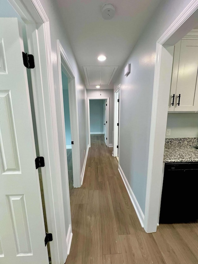 hallway with light wood finished floors, attic access, and baseboards