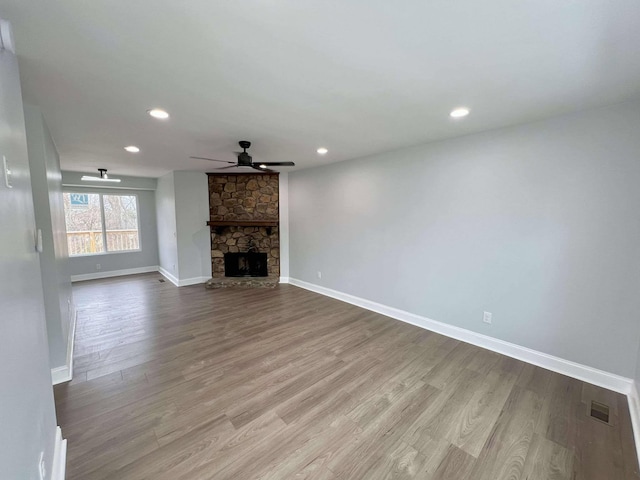 unfurnished living room featuring visible vents, ceiling fan, a stone fireplace, wood finished floors, and baseboards