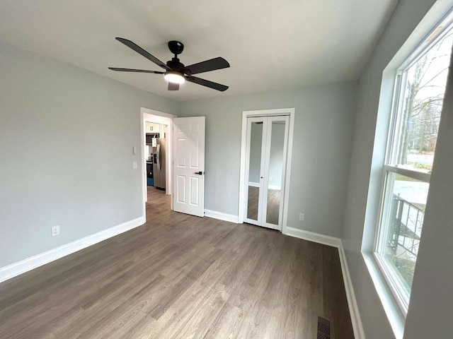 unfurnished bedroom featuring wood finished floors, visible vents, baseboards, a closet, and stainless steel refrigerator with ice dispenser