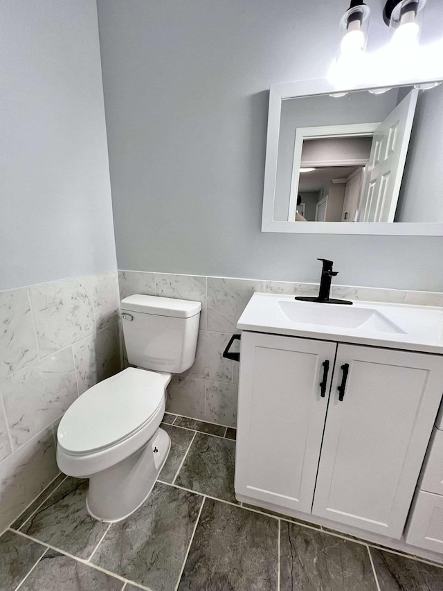 bathroom with tile walls, wainscoting, vanity, and toilet