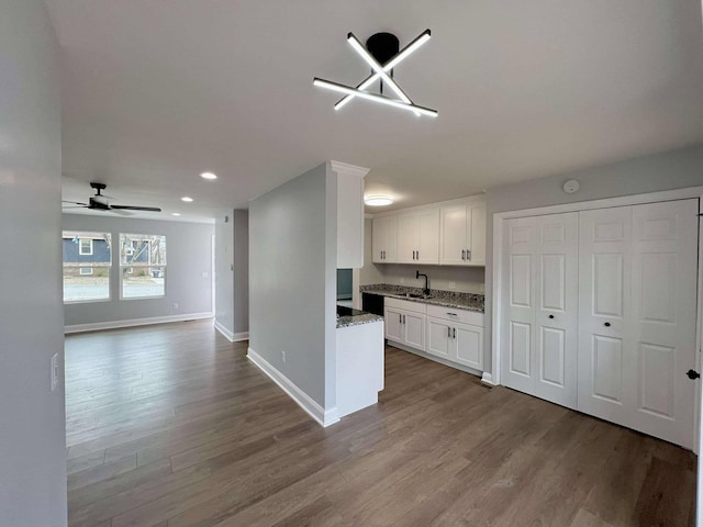 kitchen with stone counters, white cabinets, a sink, and wood finished floors