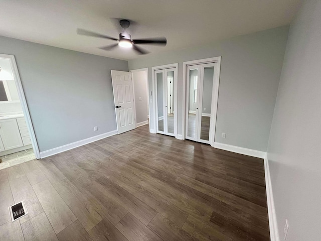 unfurnished bedroom featuring multiple closets, visible vents, ensuite bath, wood finished floors, and baseboards