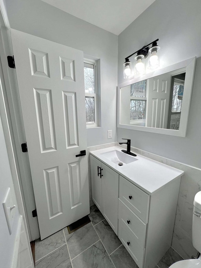 half bathroom with toilet, marble finish floor, and vanity