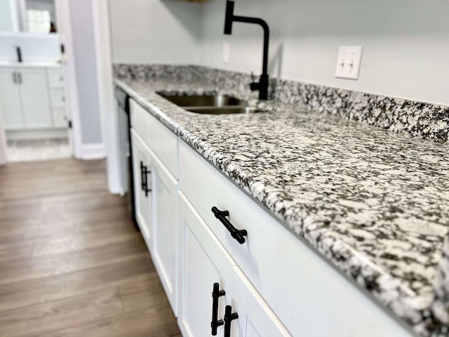 details featuring light stone countertops, white cabinetry, a sink, and wood finished floors