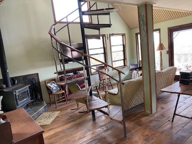 living area featuring lofted ceiling, a wood stove, stairway, and hardwood / wood-style flooring