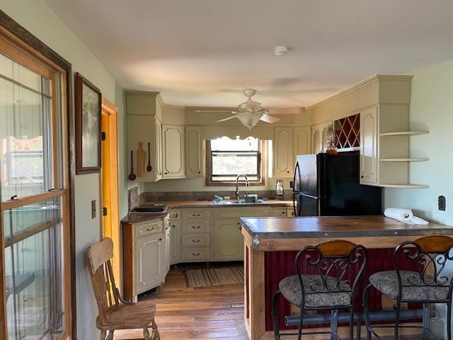 kitchen featuring a breakfast bar, freestanding refrigerator, a sink, wood finished floors, and a peninsula