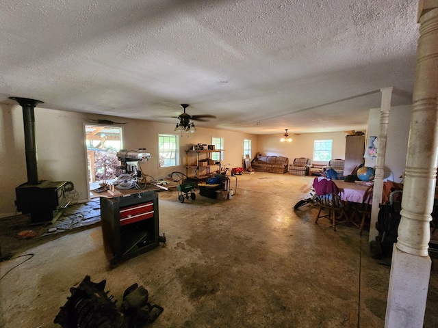 interior space with a wood stove, concrete floors, a ceiling fan, and a textured ceiling