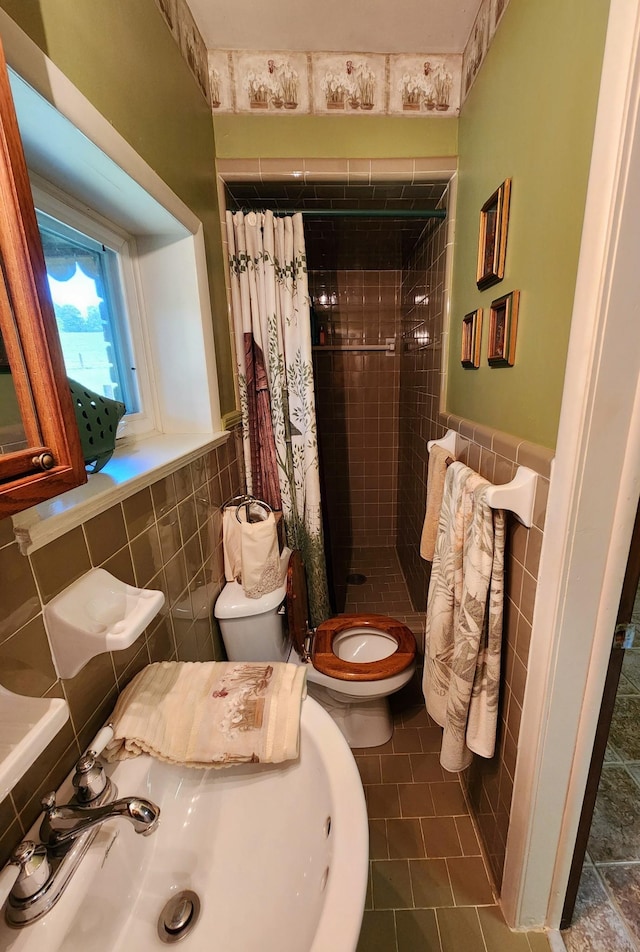 bathroom featuring tile walls, toilet, wainscoting, a sink, and a shower stall