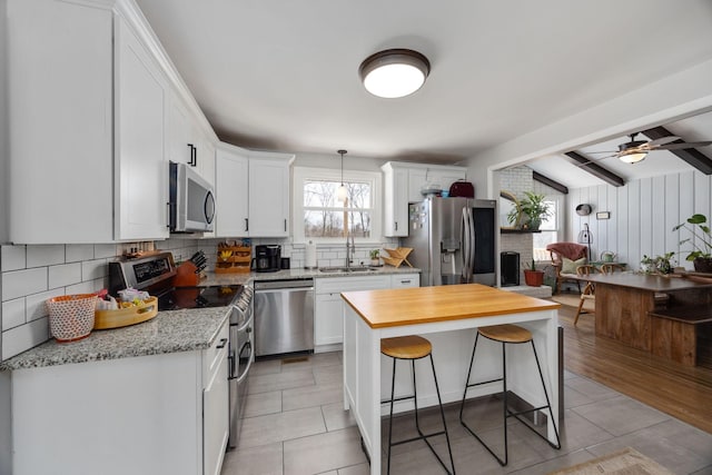 kitchen with a breakfast bar area, decorative backsplash, appliances with stainless steel finishes, white cabinetry, and a sink