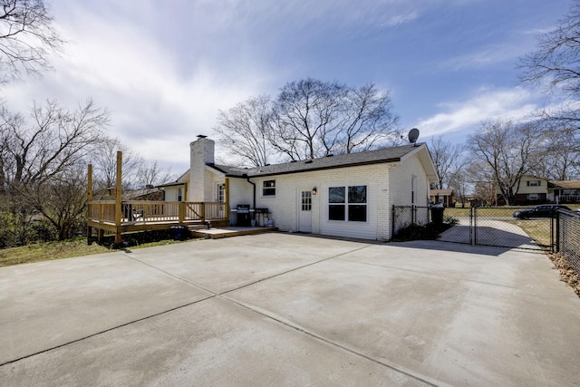 back of property with driveway, fence, a wooden deck, brick siding, and a chimney