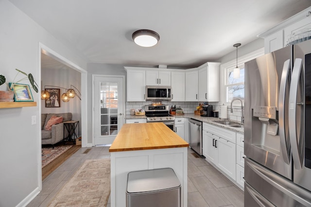 kitchen featuring a sink, butcher block countertops, appliances with stainless steel finishes, white cabinetry, and backsplash