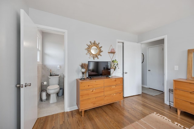 bedroom featuring tile walls, ensuite bathroom, and wood finished floors