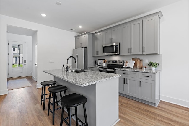 kitchen with a breakfast bar, a sink, appliances with stainless steel finishes, gray cabinets, and an island with sink