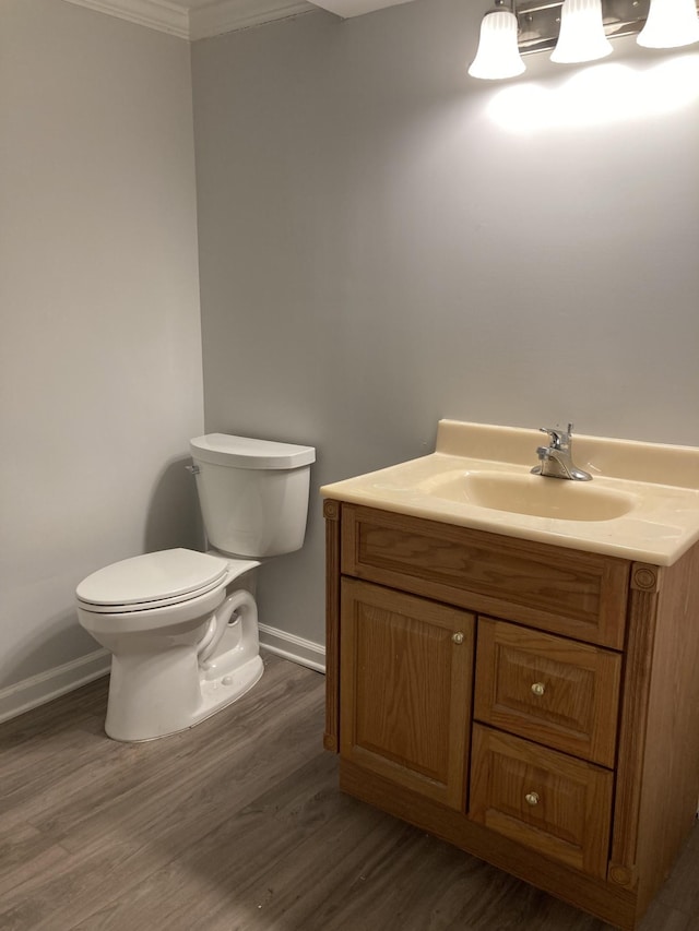 bathroom featuring crown molding, toilet, vanity, wood finished floors, and baseboards