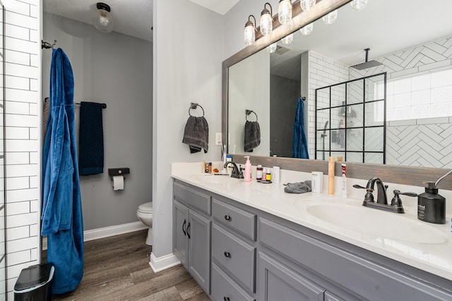 full bath featuring a tile shower, wood finished floors, a sink, and toilet