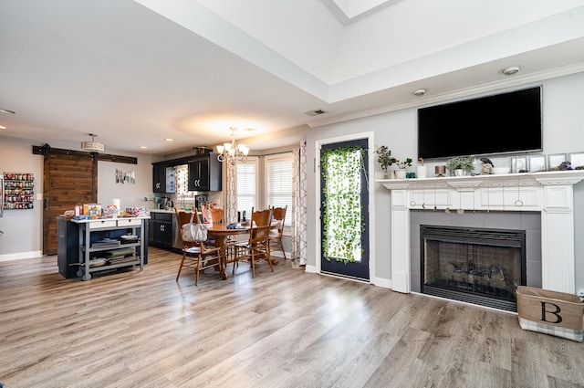 living area featuring a tiled fireplace, a barn door, light wood-type flooring, and baseboards