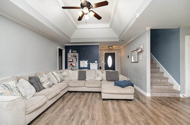 living room featuring a tray ceiling, crown molding, ceiling fan, wood finished floors, and stairs