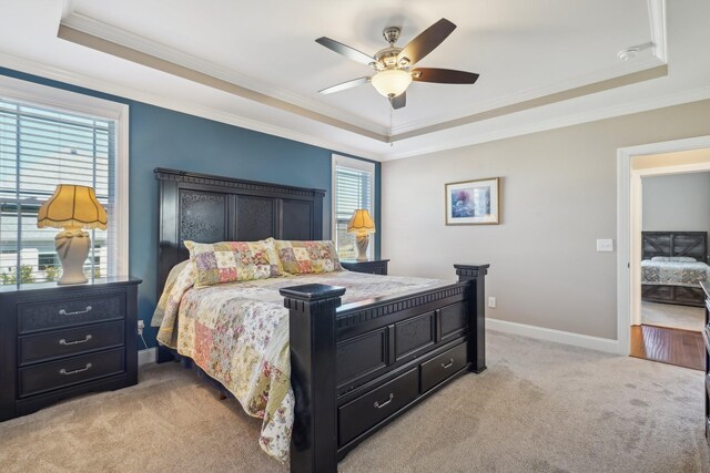 bedroom featuring ornamental molding, a tray ceiling, light carpet, and baseboards