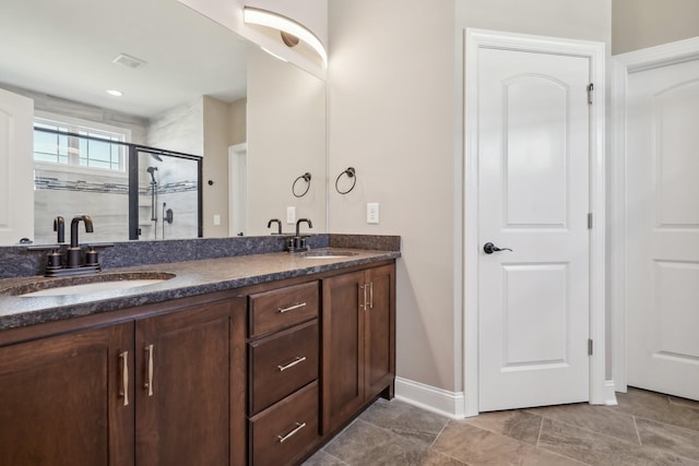 bathroom with double vanity, a shower stall, baseboards, and a sink