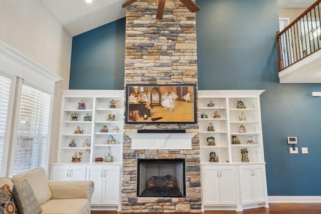 living area with high vaulted ceiling, a stone fireplace, baseboards, and wood finished floors