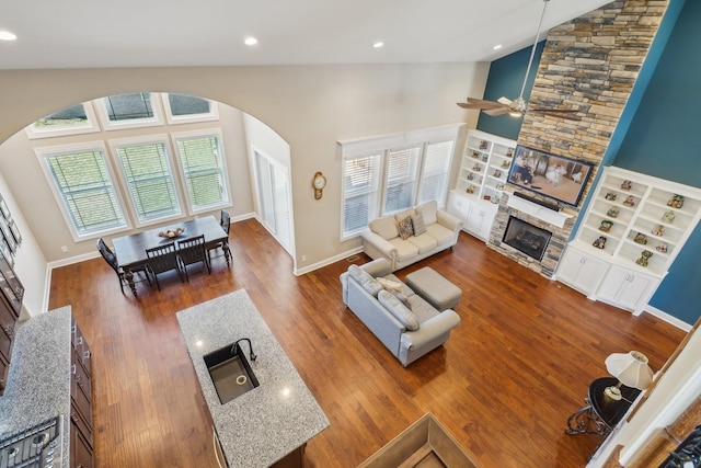 living room with arched walkways, plenty of natural light, a stone fireplace, and wood finished floors