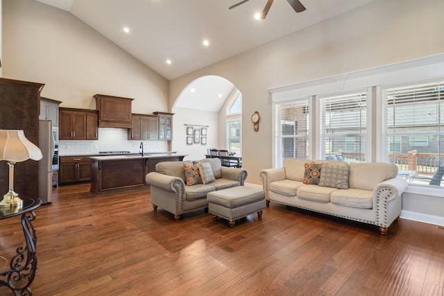 living room featuring arched walkways, dark wood-style flooring, ceiling fan, high vaulted ceiling, and baseboards