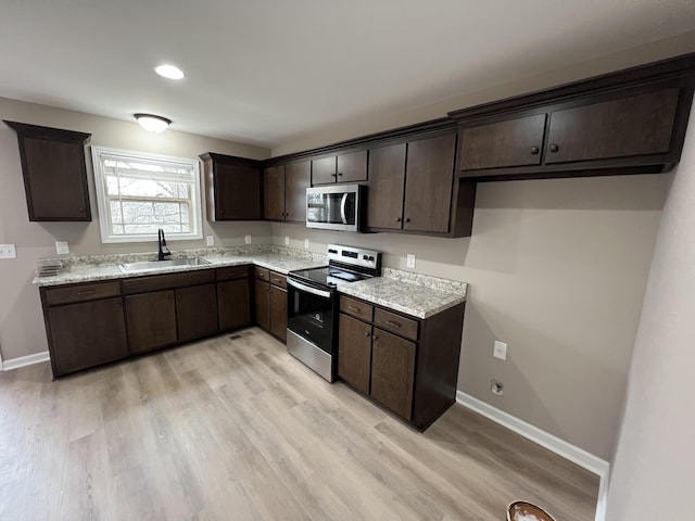 kitchen featuring baseboards, light wood-style flooring, stainless steel appliances, dark brown cabinets, and a sink