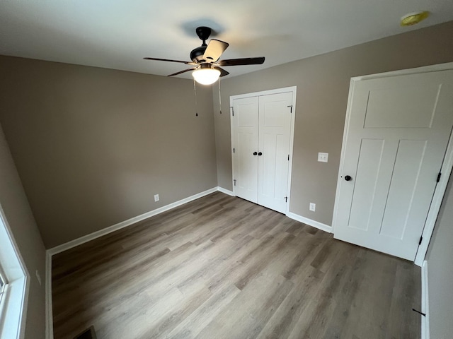 unfurnished bedroom featuring a closet, wood finished floors, a ceiling fan, and baseboards