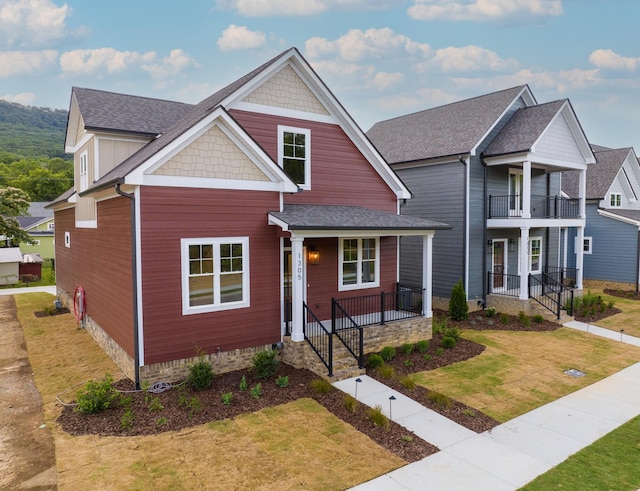 view of front of house with a balcony, roof with shingles, a porch, and a front yard