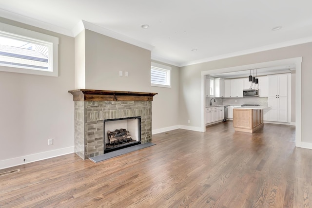 unfurnished living room featuring a fireplace with raised hearth, wood finished floors, visible vents, and crown molding