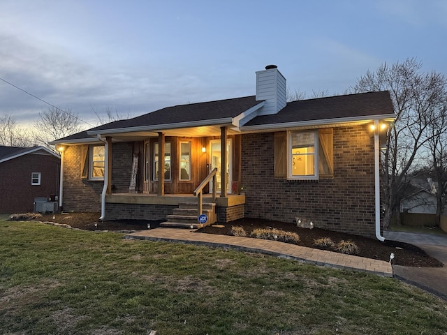 view of front facade with covered porch, brick siding, a lawn, and a chimney