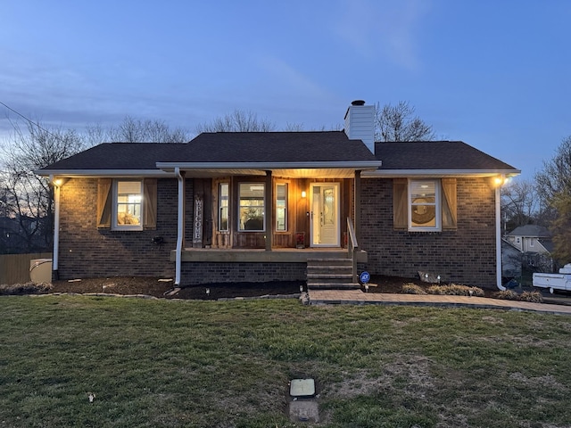 view of front facade with brick siding, roof with shingles, a chimney, covered porch, and a front yard