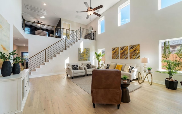 living area with baseboards, stairway, a high ceiling, light wood-style floors, and a ceiling fan