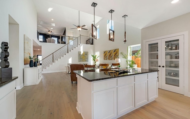 kitchen with light wood finished floors, pendant lighting, dark stone countertops, a towering ceiling, and white cabinets