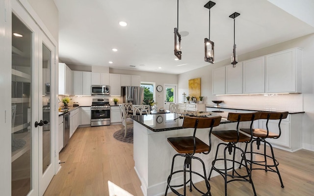 kitchen with a breakfast bar, light wood-style flooring, dark countertops, tasteful backsplash, and appliances with stainless steel finishes