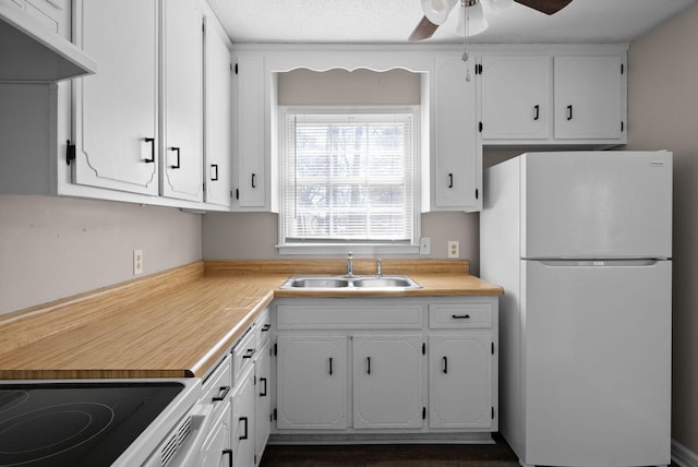 kitchen with under cabinet range hood, white cabinetry, a sink, and freestanding refrigerator