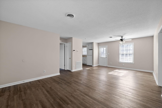 unfurnished living room featuring a textured ceiling, dark wood-style flooring, visible vents, and baseboards