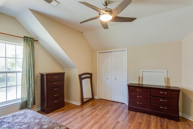 bedroom with a closet, visible vents, light wood-style flooring, vaulted ceiling, and baseboards