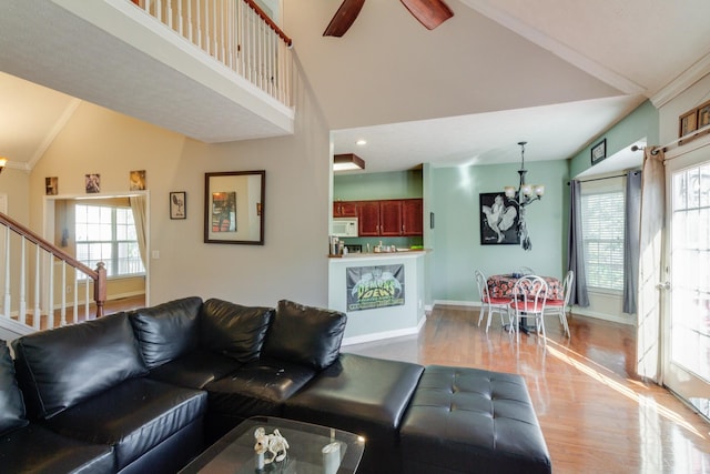 living room with baseboards, light wood-style flooring, stairs, high vaulted ceiling, and ceiling fan with notable chandelier