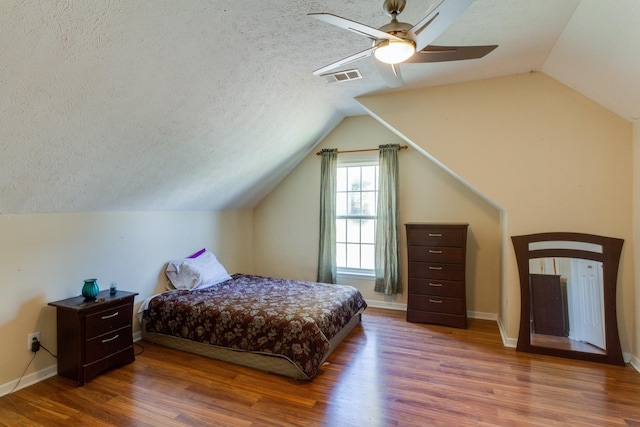 bedroom with a textured ceiling, visible vents, vaulted ceiling, and wood finished floors