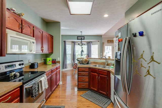 kitchen featuring light wood-style flooring, decorative light fixtures, a peninsula, stainless steel appliances, and a sink