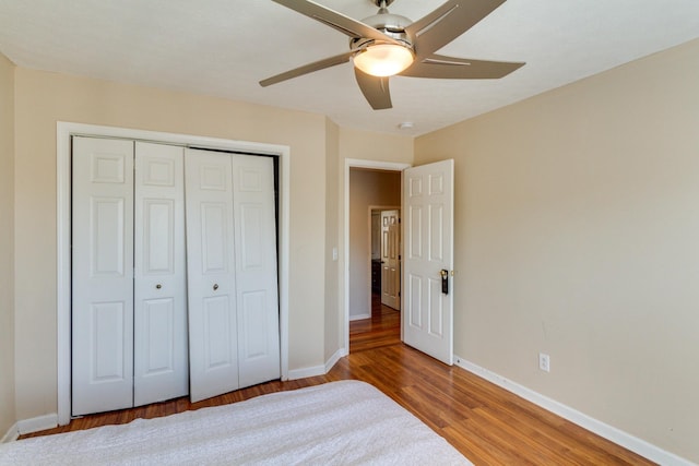 unfurnished bedroom with ceiling fan, a closet, wood finished floors, and baseboards