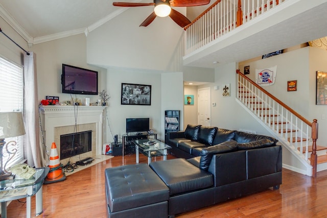 living area featuring a tiled fireplace, ceiling fan, wood finished floors, stairs, and crown molding