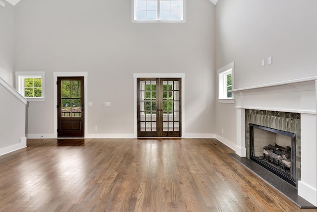 unfurnished living room with baseboards, a towering ceiling, wood finished floors, french doors, and a fireplace