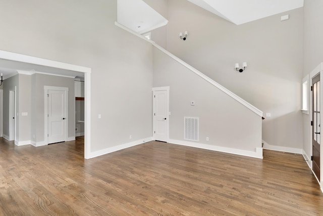 unfurnished living room with visible vents, a towering ceiling, baseboards, and wood finished floors