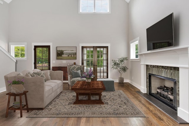 living area with french doors, a high ceiling, a tiled fireplace, wood finished floors, and baseboards