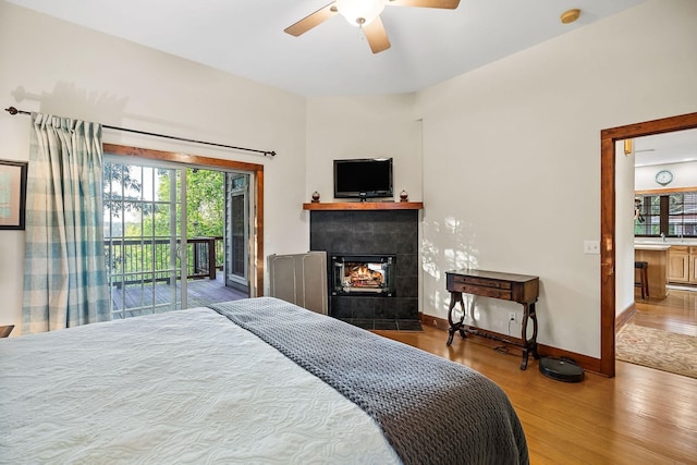 bedroom featuring access to exterior, a tiled fireplace, ceiling fan, wood finished floors, and baseboards