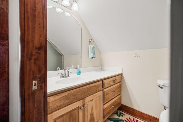 bathroom featuring lofted ceiling, baseboards, vanity, and toilet