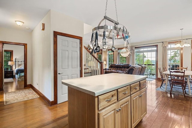 kitchen featuring a notable chandelier, baseboards, light countertops, a center island, and dark wood-style floors