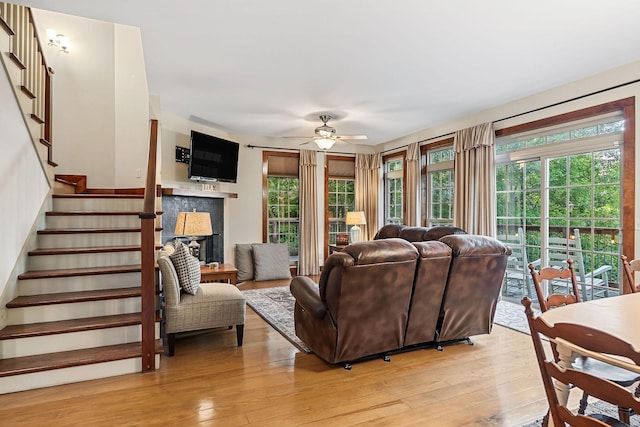 living room featuring light wood-style flooring, stairs, ceiling fan, and a fireplace